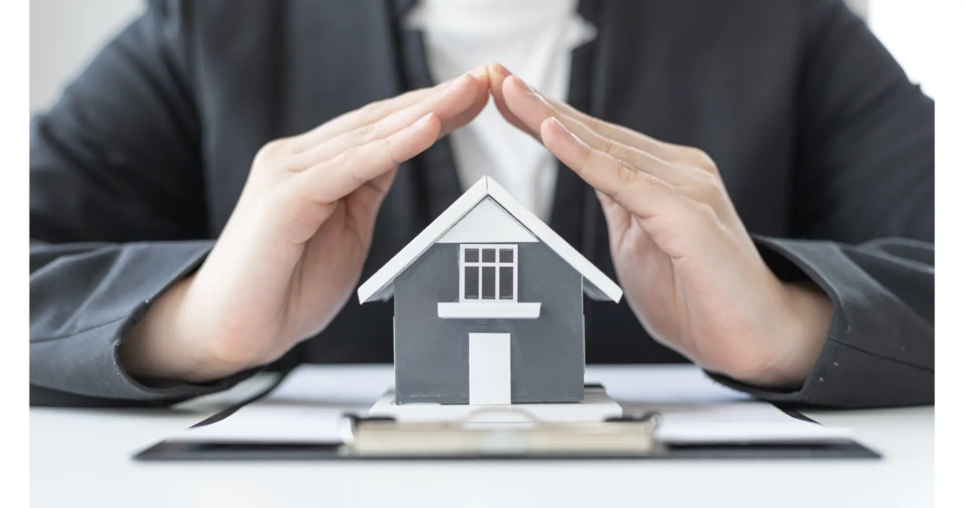 Hands forming a protective roof over a model house